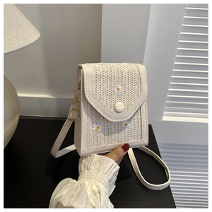 Detail of beige straw crossbody bag with daisy embroidery and round button closure