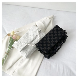 Close-up of checkerboard embossed crossbody bag with chunky chain strap on white suit