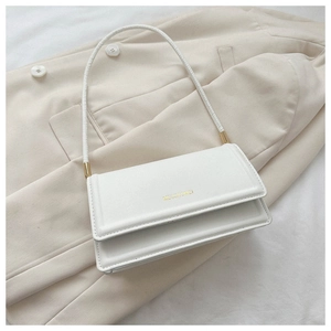 Detailed view of white faux leather shoulder bag with golden logo on beige blazer