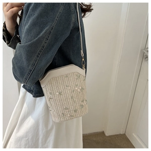 Detail of woven straw bucket bag with green floral embroidery and white leather strap