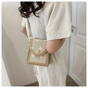 Detail of straw woven crossbody bag with daisy embroidery and leather trim on a model
