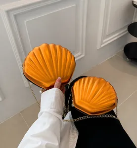 Detail of orange shell-shaped chain bags with metallic finish and gold strap