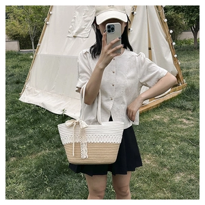 Detail of woven straw tote bag with cream lace bow and contrast stitching