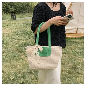 Close-up of woven straw tote bag featuring green spiral accents and a white lace bow