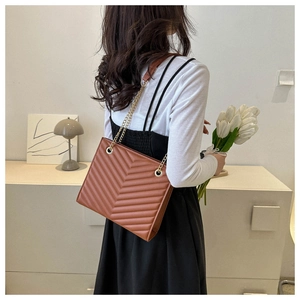 Side view of a brown faux leather tote with V-quilt pattern and gold chain strap on model