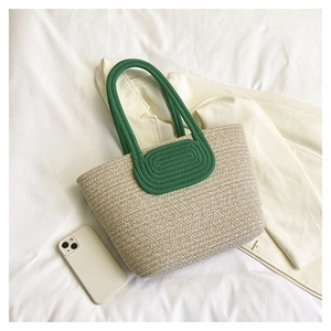 Detail of hand-woven straw tote bag with green rope handles on white fabric backdrop