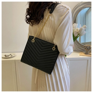 Detail of black quilted shoulder bag with gold chain strap on a white dress model