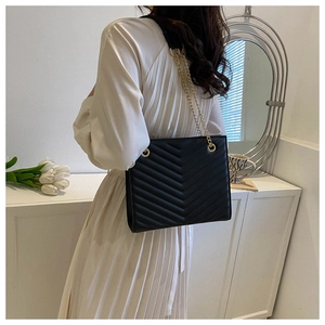 Detail of black chevron quilted shoulder bag with golden chain strap on white dress