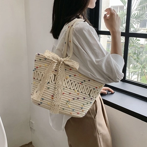 Beige woven straw tote bag with colorful dots and a large white lace bow for summer beach