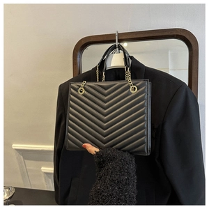 Close-up of black quilted leather tote bag with V-shaped stitching and gold chain strap