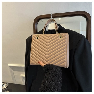Detail showing beige V-quilted texture with gold chain strap on women's shoulder bag