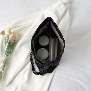 Minimalist black quilted shoulder bag with chunky chain strap on elegant white fabric