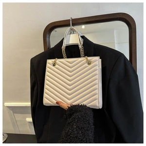 Detail of V-quilted faux leather texture and gold chain strap on cream shoulder bag