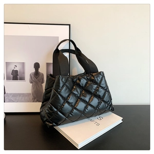 Détail d'un sac cabas noir matelassé avec finition brillante sur un bureau épuré