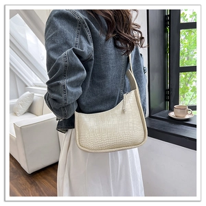 Detail shot of the cream crocodile pattern shoulder bag on a model in a sunlit room