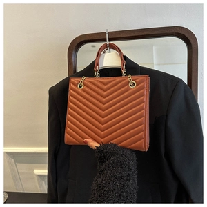 Detail of caramel quilted handbag featuring V-pattern stitching and gold chain hardware