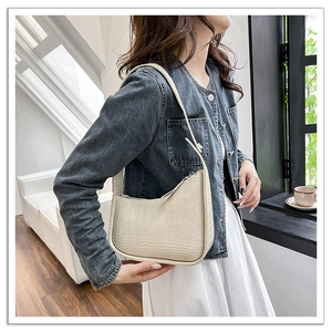 Detail of cream faux crocodile texture hobo bag worn by model in a modern interior