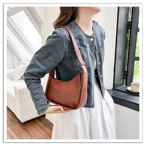 Detailed side view of a brown crocodile pattern half-moon shoulder bag on a model