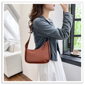 Brown crocodile embossed hobo shoulder bag styled on model in a modern living room setup
