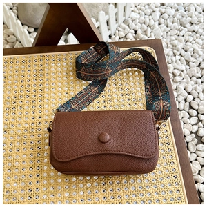 Close-up of vintage brown crossbody bag with colorful ethnic style wide strap and leather grain