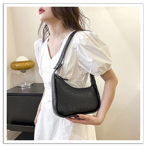 Model wearing a black crocodile embossed hobo bag with adjustable strap and zip closure