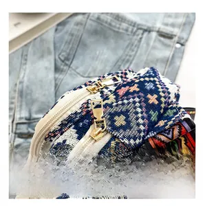 Close-up of smooth dual golden zippers on bohemian woven crossbody bag over denim fabric