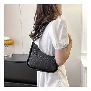 Detail of black faux crocodile skin hobo bag worn over the shoulder on a white dress