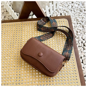 Detail of vintage brown textured leather bag with colorful ethnic style wide strap