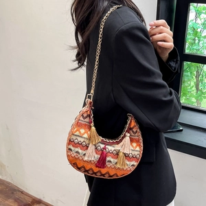 Close-up of ethnic woven crescent bag with colorful tassels and gold chain strap detail