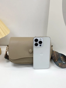 Close-up of beige lychee texture shoulder bag with ethnic patterned wide strap and phone