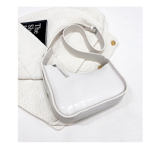 Detail of white crocodile pattern leather shoulder bag with adjustable strap on tweed background