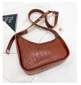 Detail of brown crocodile pattern hobo bag with adjustable silver buckle on a tweed jacket