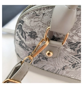 Detail of embroidered fabric with crane pattern and gold-tone metal hardware on handbag