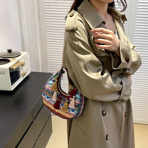 Close-up of ethnic crescent bag with colorful embroidery and tassels worn over a trench coat