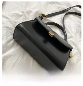 Detail of black leather crossbody bag featuring vintage gold clasp and thin strap
