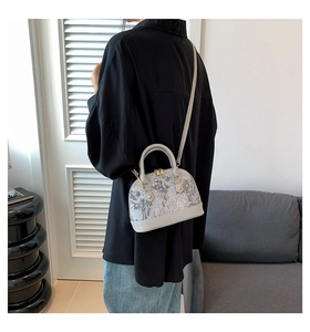 Rear view of a model wearing a small grey shell shoulder bag with embroidered details