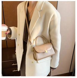 Detail of a beige glossy leather crossbody bag with minimalist gold metal buckle closure