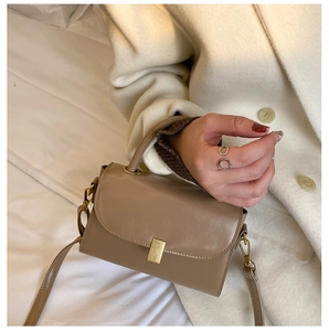 Close-up of small square bag with golden buckle on a white wool coat background
