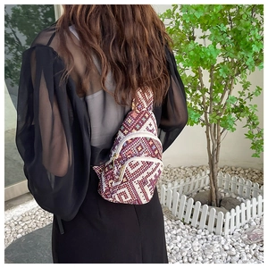 Ethnic style woven chest bag with geometric patterns shown on a model in a garden