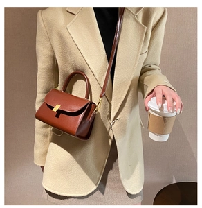 Close-up of elegant brown leather bag with gold buckle on a beige winter coat