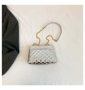 Détail du sac argenté matelassé avec bandoulière chaîne sur fond de costume gris