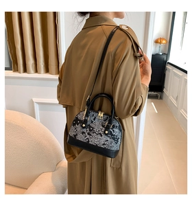 Detail of black shell-shaped leather bag with white embroidery and golden metal accents