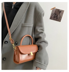 Detail of a brown leather crossbody bag with a gold buckle and adjustable thin strap
