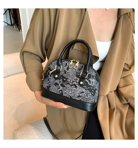Close-up of black shell bag with white embroidery and golden metal hardware on a trench coat