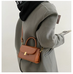 Detail of a brown synthetic leather square handbag with golden clasp and slim shoulder strap