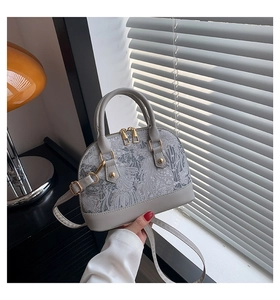 Detail of grey shell bag with floral embroidery and golden zipper hardware accents