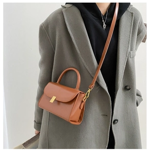 Caramel brown small square bag with golden hardware shown as crossbody on a model