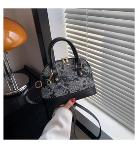 Detail of black shell-shaped handbag featuring elegant wave embroidery and golden rivets