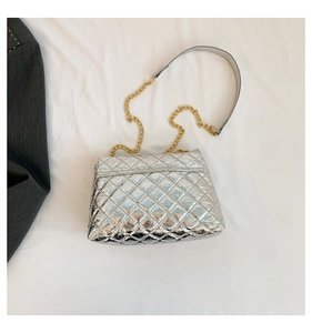 Gros plan sur un sac argenté matelassé avec chaîne dorée sur un tissu blanc fluide