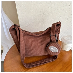Close-up of brown corduroy crossbody bag texture and small round pouch on a wooden table